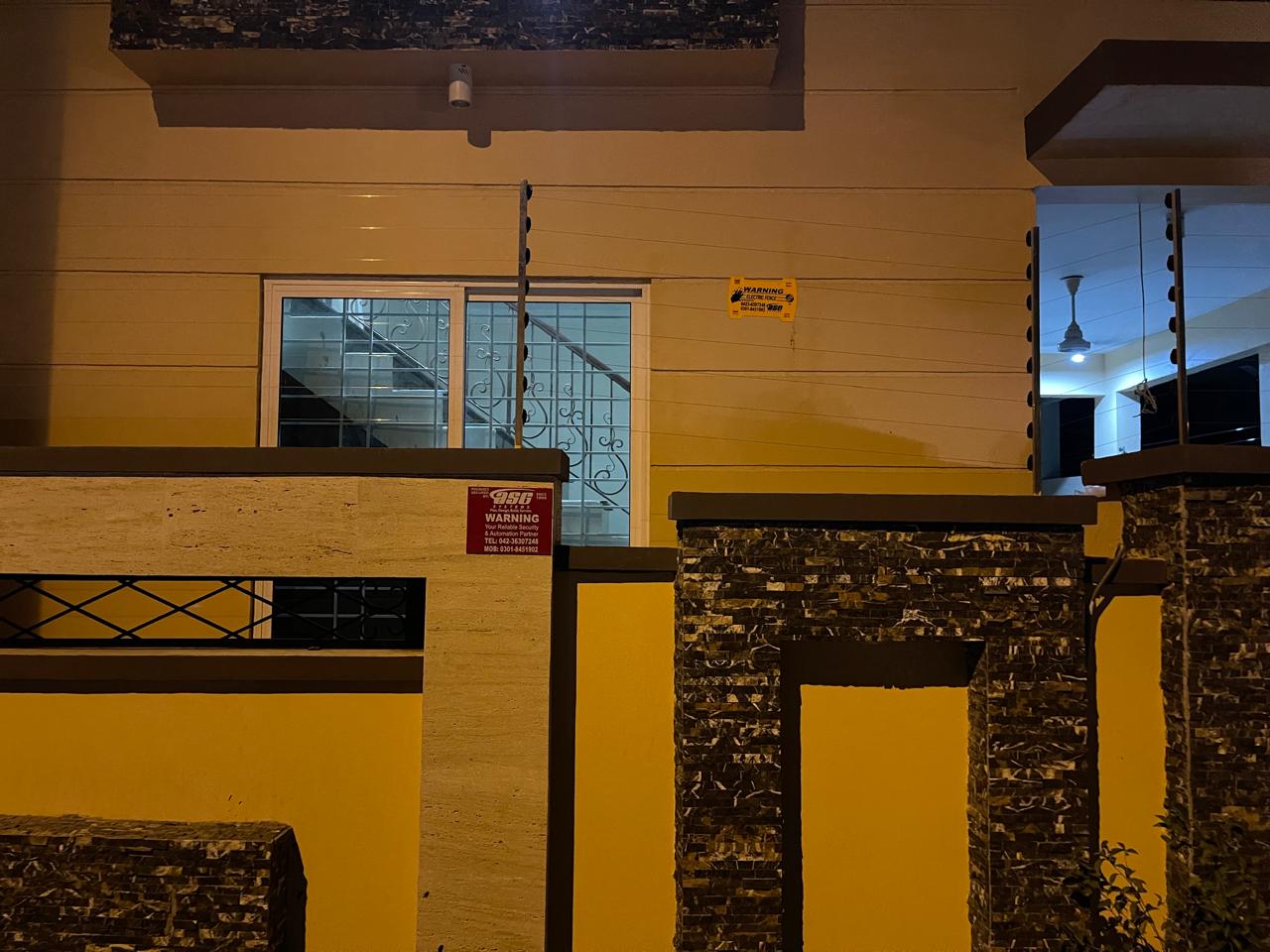 Wall-top electric fence with a warning sign on a modern house with stone cladding