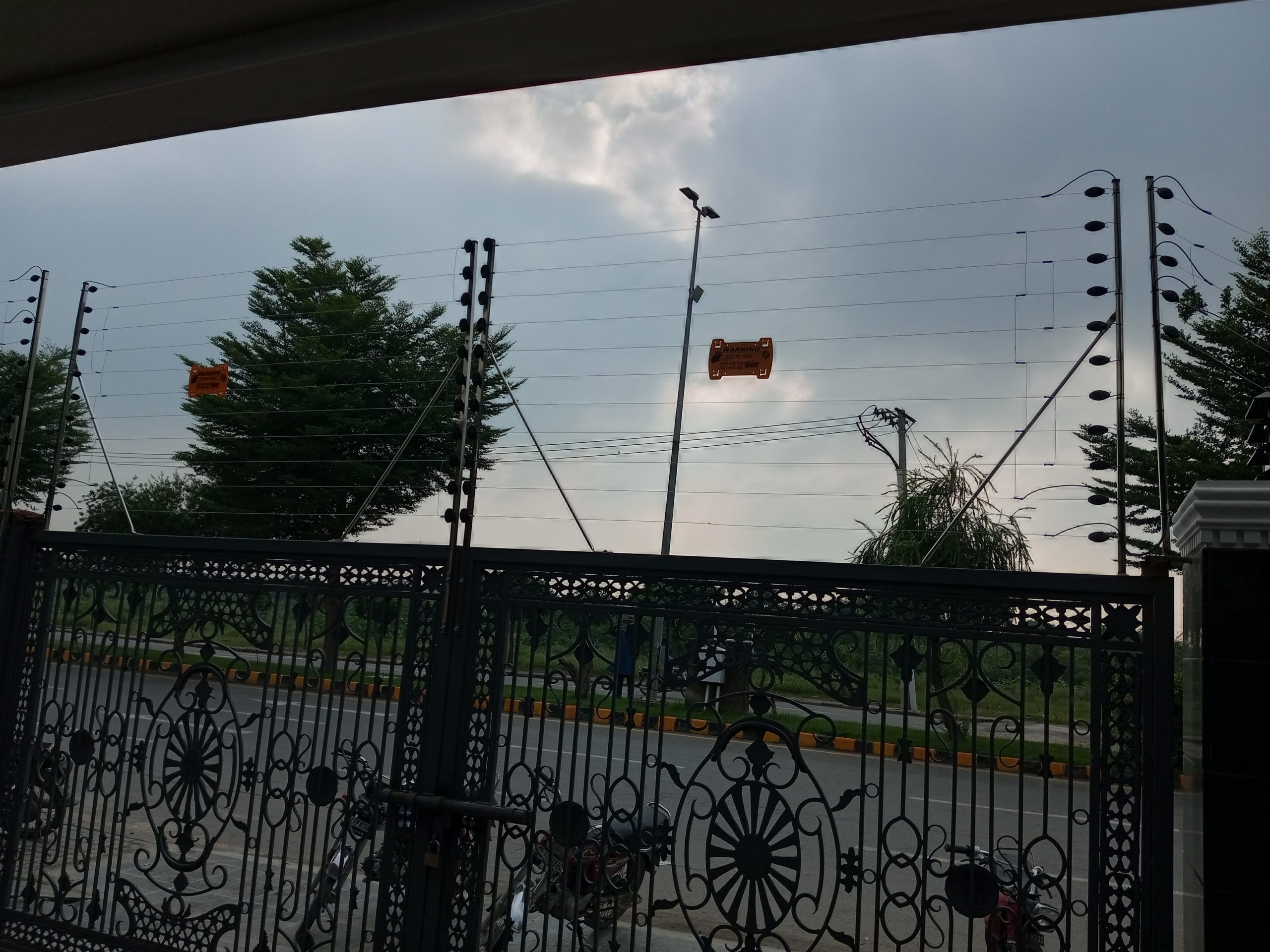 Multi-strand electric fence with warning signs installed on the boundary wall and main gate of a home in Pakistan