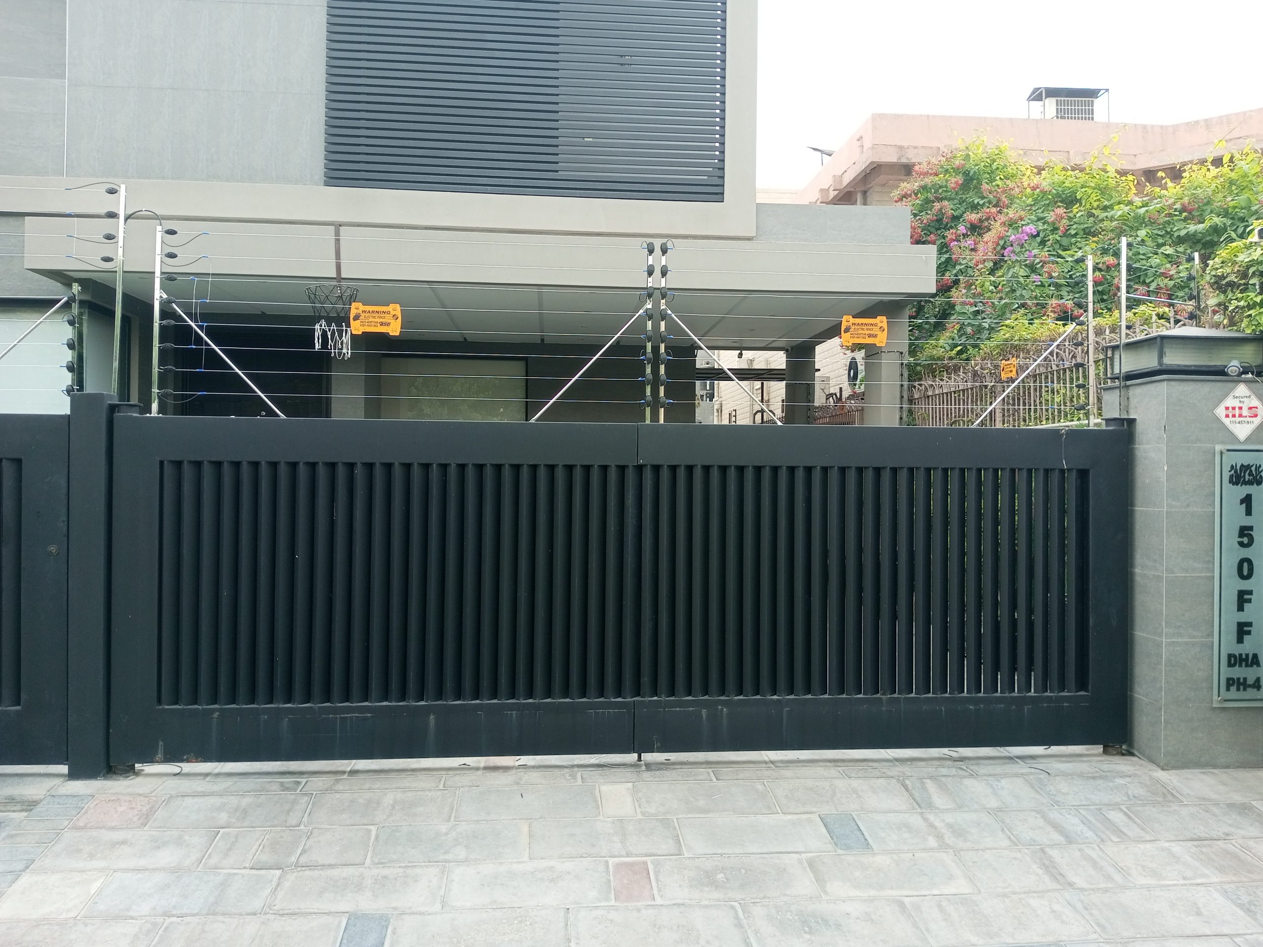 Electric fence with warning signs installed on the boundary wall and gate of a modern house