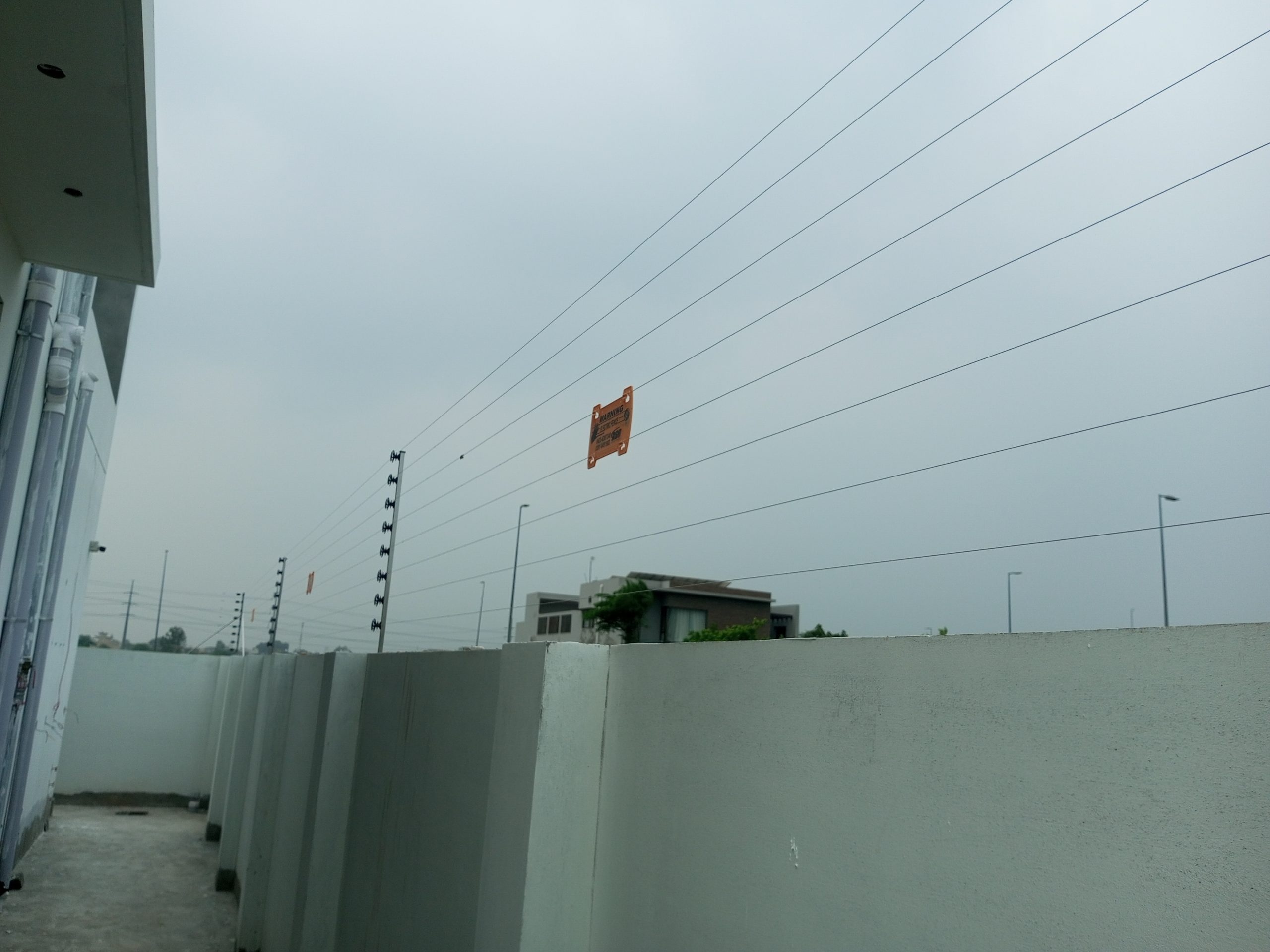 Multi-strand electric fence running along the top of a high boundary wall under the sky