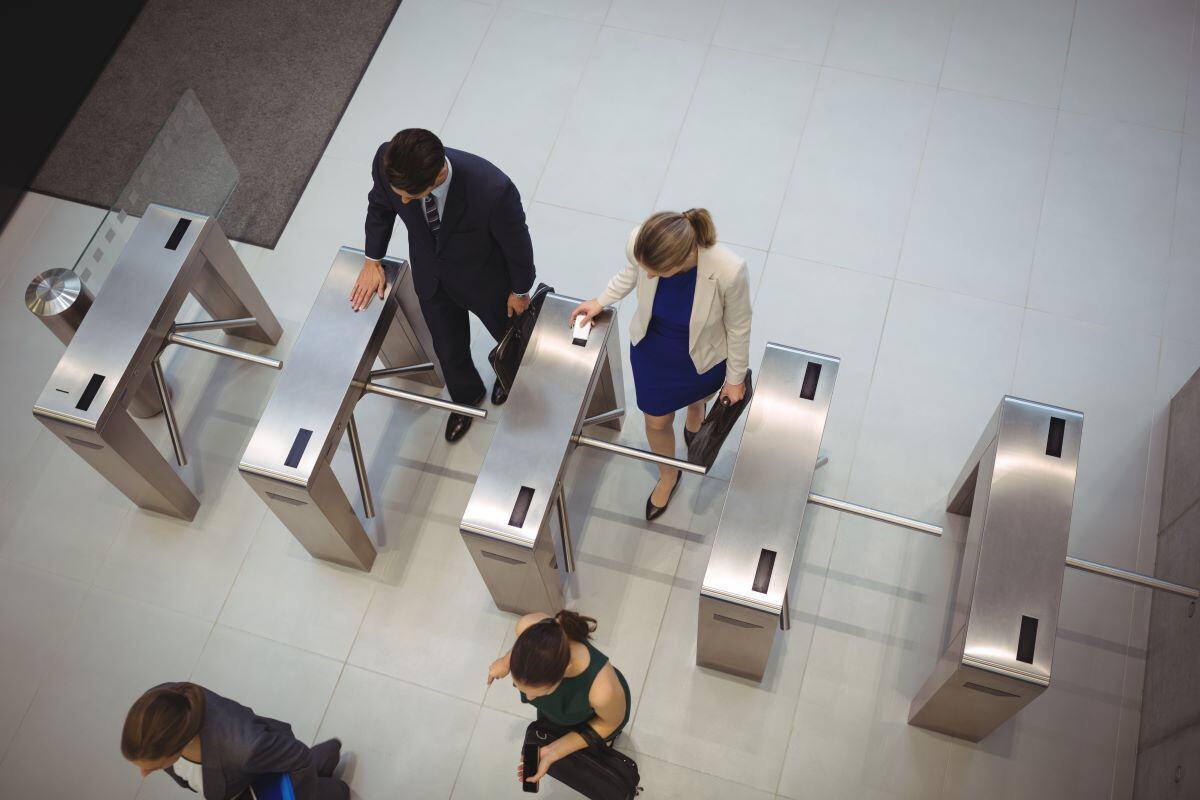 Top view of people passing through stainless steel tripod turnstiles in an office entrance